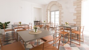 A dining area with multiple tables and chairs, a potted plant, and a large window with a view. - Dimora Cummà Marì (Vieste)
