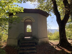 Ein kleines, rustikales Gebäude mit einer Steinaußenwand, einem Bogenportal und einer Tafel, die auf seine historische Bedeutung hinweist.