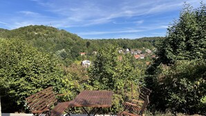 Une terrasse avec une table et des chaises, donnant sur une colline où se trouvent des maisons.