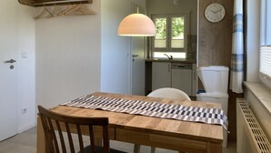 Un coin repas avec une table en bois, un luminaire suspendu et une vue sur la cuisine.