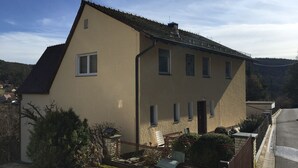 Une maison à deux étages, dotée d’un toit en pente, de nombreuses fenêtres et d’un petit jardin clos.