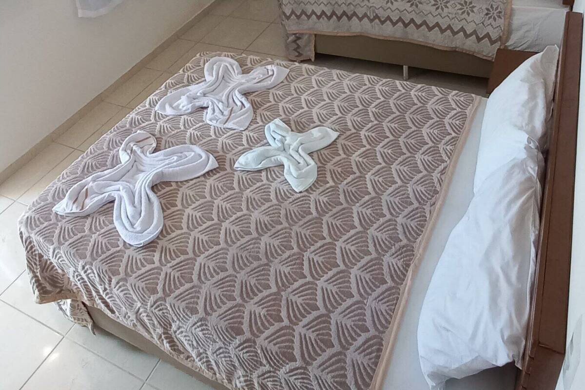 Habitación de hotel con dos camas, ventilador de techo, ventana con cortinas y piso de baldosas.