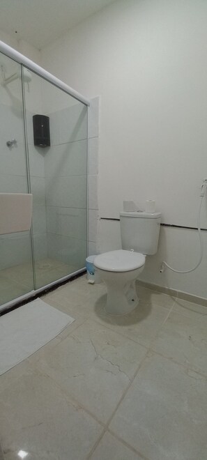 A bathroom with a toilet, a glass shower enclosure, and a tiled floor.