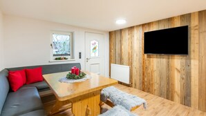 Un soggiorno moderno con pavimento in legno, un divano grigio, cuscini rossi, un tavolo da pranzo in legno con candele e una TV a parete.