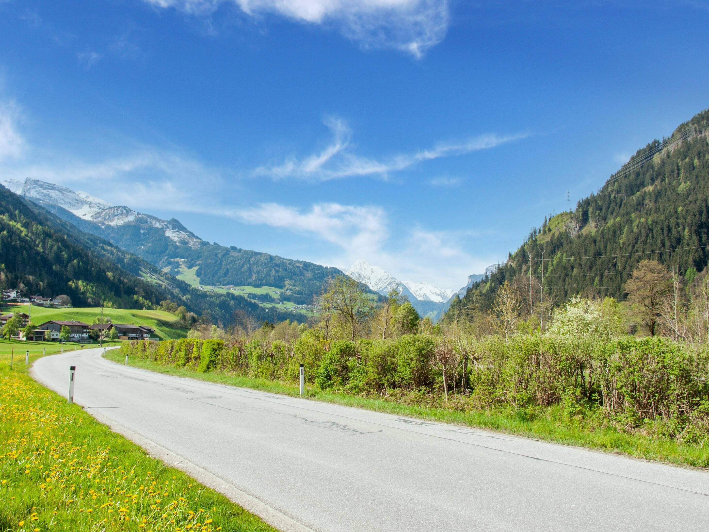 A rural road curving through a valley with mountains in the background.