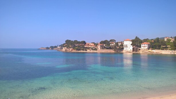 A coastal town with clear blue waters, buildings with red roofs, and a beach.