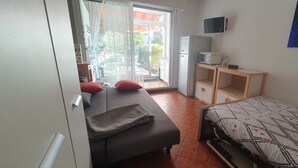 A bedroom with a bed, a desk, a chair, a television, and a view of the outside.