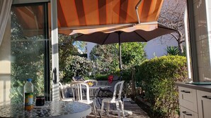 An outdoor patio with a table, chairs, a grill, and a large umbrella.