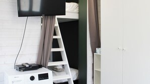 A room with a white wardrobe, a white shelf, a white ladder, a flat-screen TV mounted on the wall, and a Hisense washing machine. - Nice studio  - 2P - near Paris (Ivry-sur-Seine)
