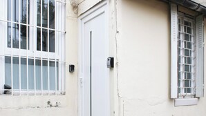 A white door with a vertical handle, flanked by two windows with white frames and metal bars. - Nice studio  - 2P - near Paris (Ivry-sur-Seine)