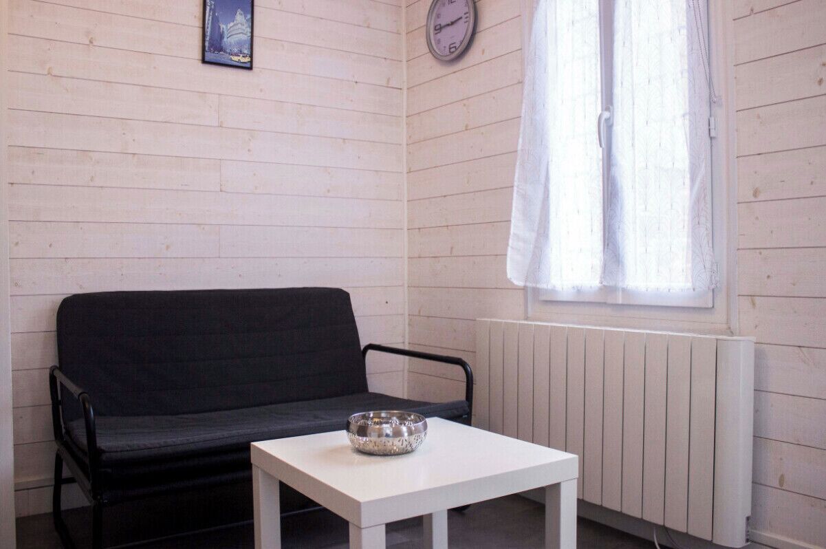 A room with a black sofa, a white table with a bowl, a clock, and a window with curtains.