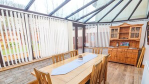 Une véranda avec une table et des chaises en bois, un mur en briques et un buffet en bois doté de portes en verre.