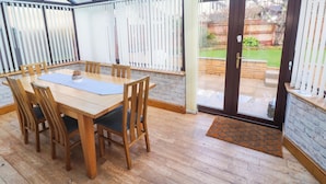 Une véranda avec une table et des chaises en bois, une porte vitrée donnant sur l’extérieur et un mur en briques.