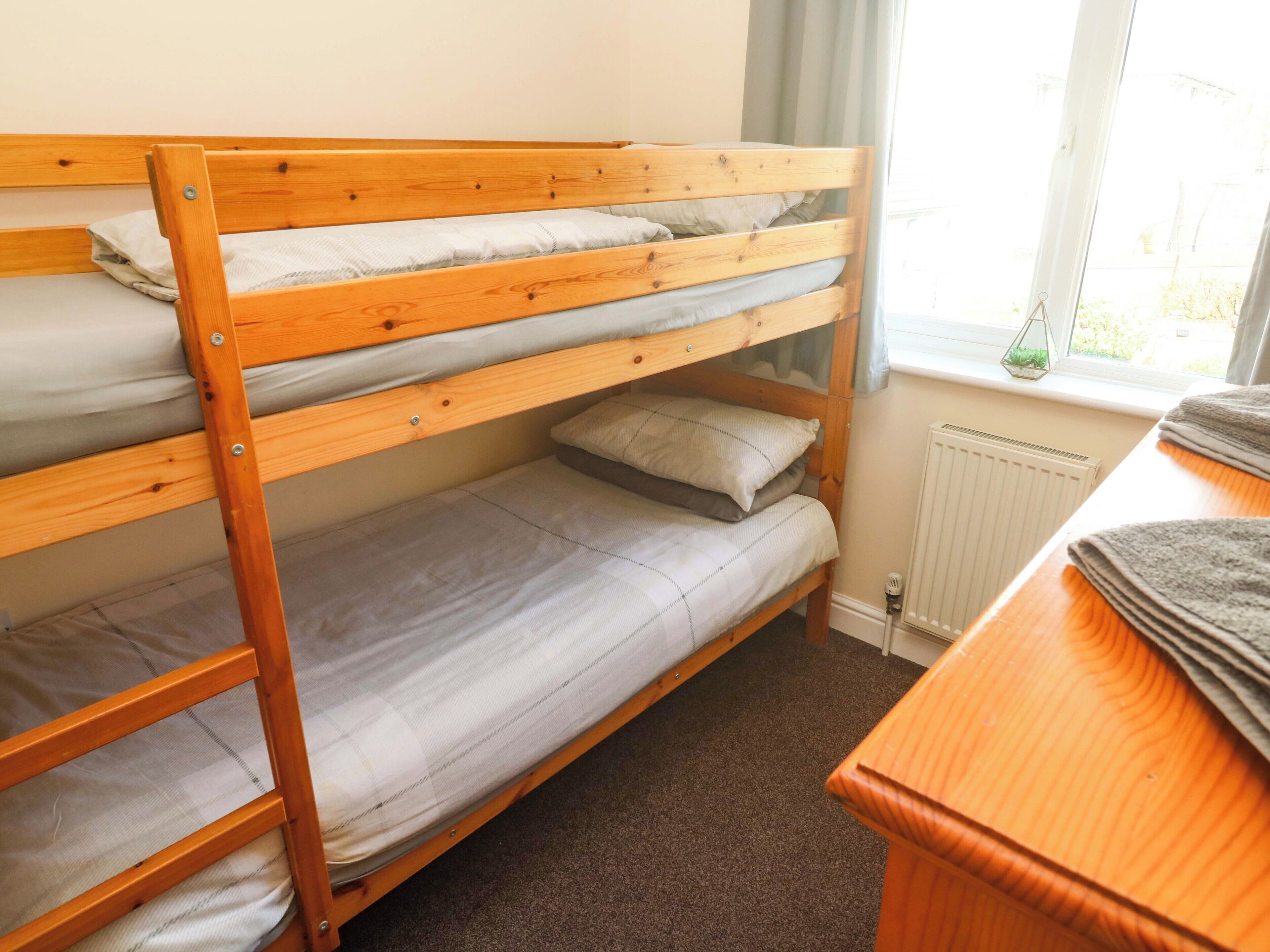 A bunk bed with three levels, a radiator, and a window with curtains.