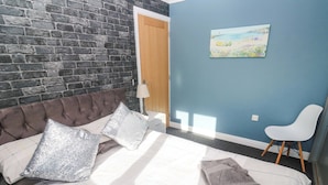 Une chambre avec un mur en briques, un lit avec des oreillers, une chaise et un tableau accroché au mur.