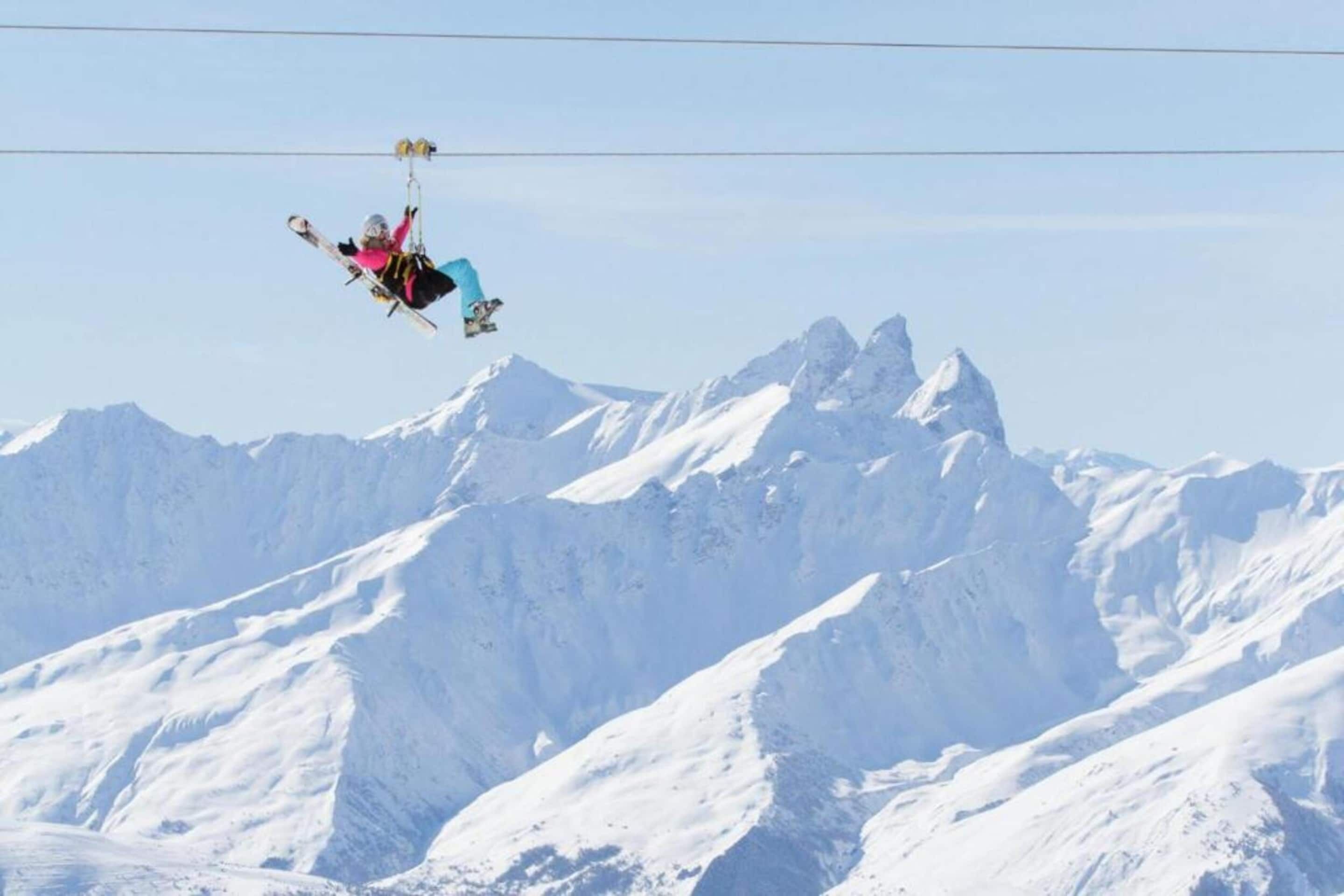 A person skiing on a cableway above snow-covered mountains.