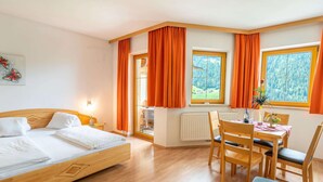 A hotel room with a bed, a dining table with chairs, and large windows with curtains. - Apartment Neustift Near Stubai Glacier (Neustift Im Stubaital)