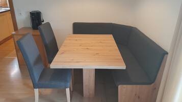 Ein Essbereich mit einem Holztisch, zwei blauen Stühlen, einer schwarzen Kaffeemaschine und einem Holzschrank.