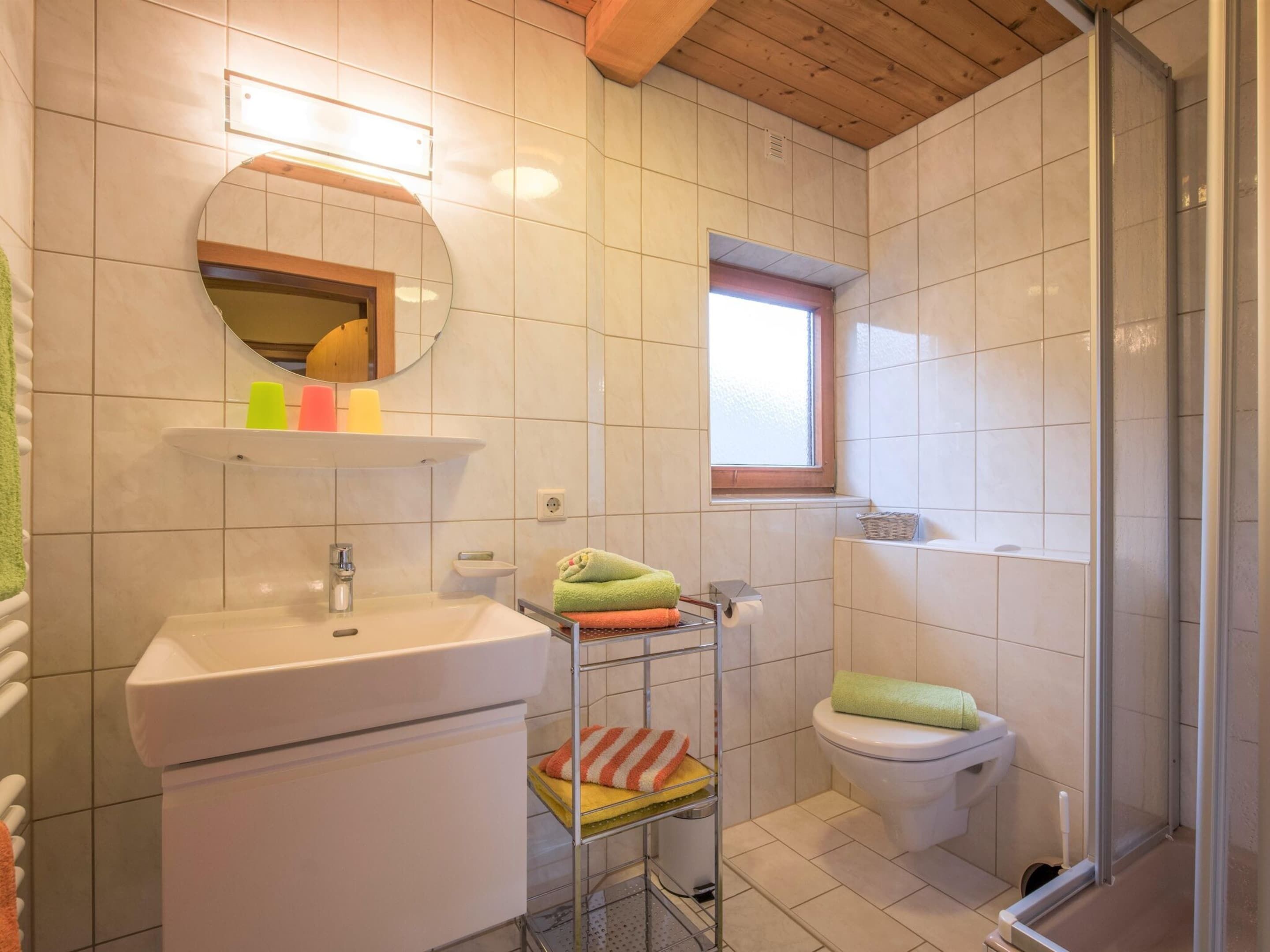 A bathroom with a sink, mirror, and toilet. There is a window providing natural light and a shower area.