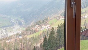 A view from a window overlooking a valley with houses, a winding road, and a mountain range. - Beautiful Apartment in a top Location in the Zillertal (Hainzenberg)