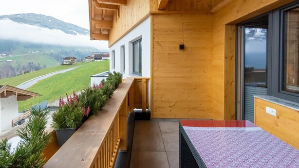 A wooden balcony with a view of a green valley and mountains. - Beautiful Apartment in a top Location in the Zillertal (Hainzenberg)