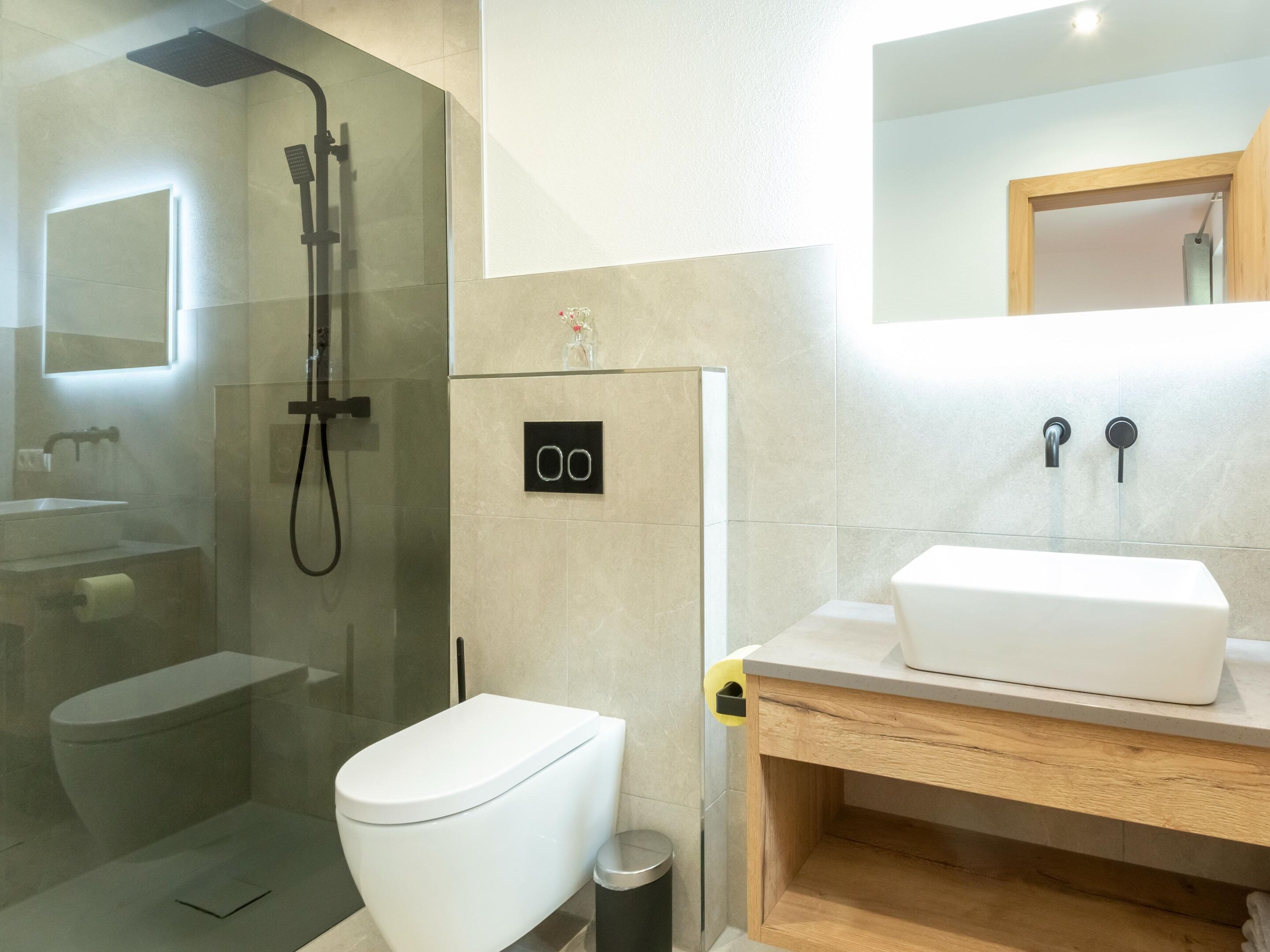 Ein modernes Badezimmer mit einer gläsernen Duschkabine, einer weißen Toilette und einem hölzernen Waschtisch.