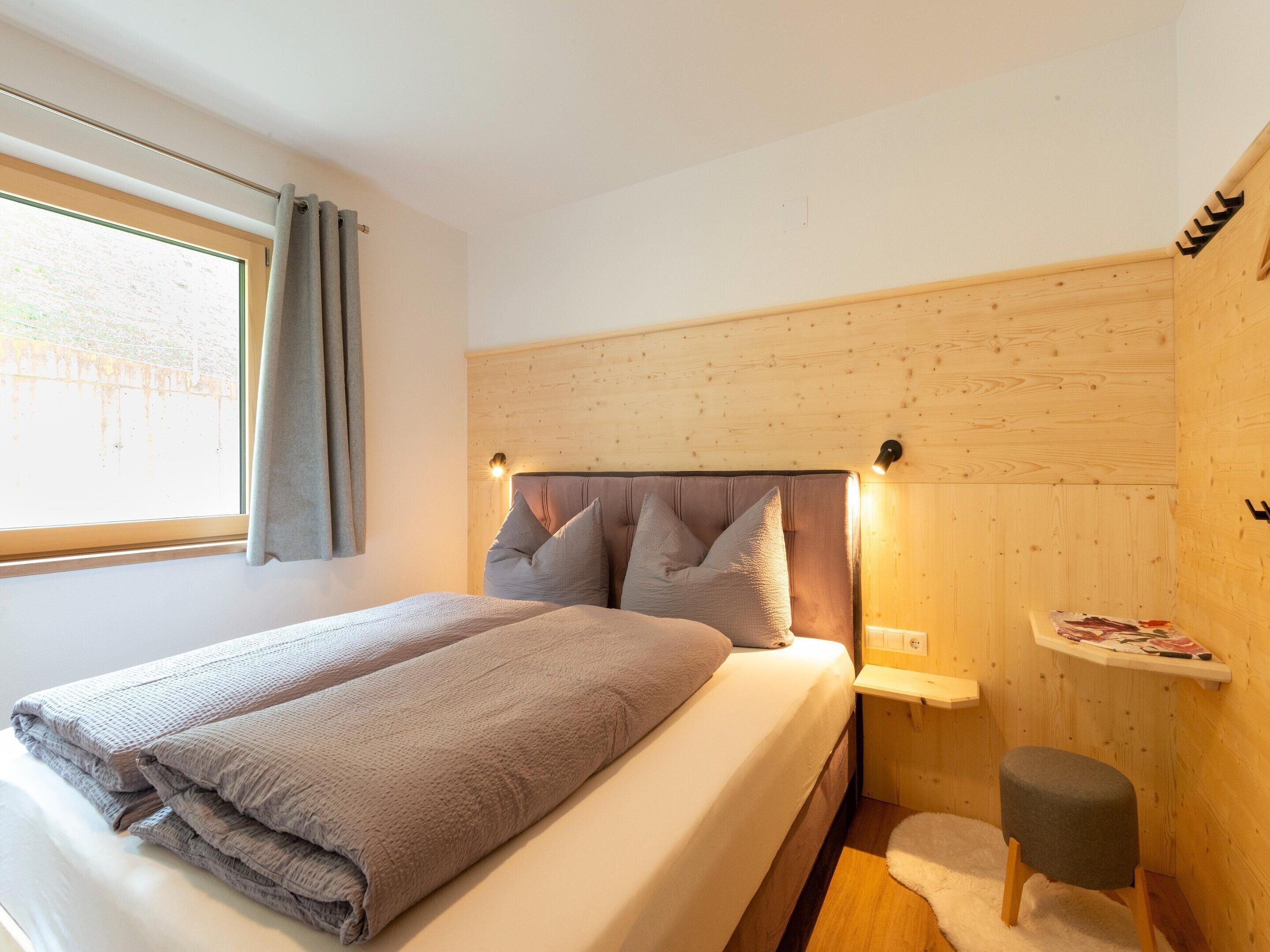 Un dormitorio con cama, mesita de noche, cortinas en la ventana y un panel de pared de madera.