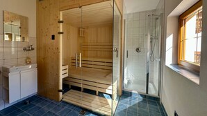 A modern bathroom with a wooden sauna, a glass-enclosed shower, and a large mirror. - Family Apartment in Neustift With Sauna and Garden (Neustift Im Stubaital)