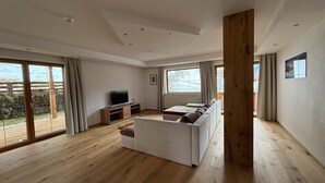 A modern living room with a sofa, a TV, and a wooden floor. - Family Apartment in Neustift With Sauna and Garden (Neustift Im Stubaital)