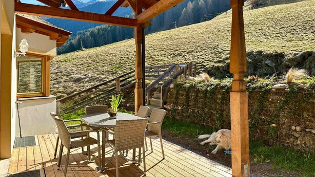 A wooden deck with wicker furniture, a glass door, and a view of a mountainous landscape. - Family Apartment in Neustift With Sauna and Garden (Neustift Im Stubaital)