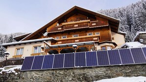A multi-story wooden chalet with a stone foundation, solar panels, and a snowy landscape. - Apartment in Hippach With Mountain Views (Hippach)