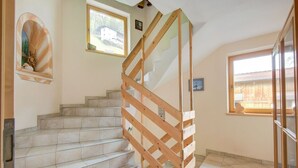 Un escalier avec des rampes en bois menant à un palier, une petite alcôve ornée d’une statue et une fenêtre donnant sur une maison.