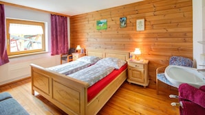 Une chambre à coucher avec une tête de lit en bois, un lit avec une literie blanche, une table de chevet avec une lampe, une chaise, une petite table et une fenêtre avec des rideaux.