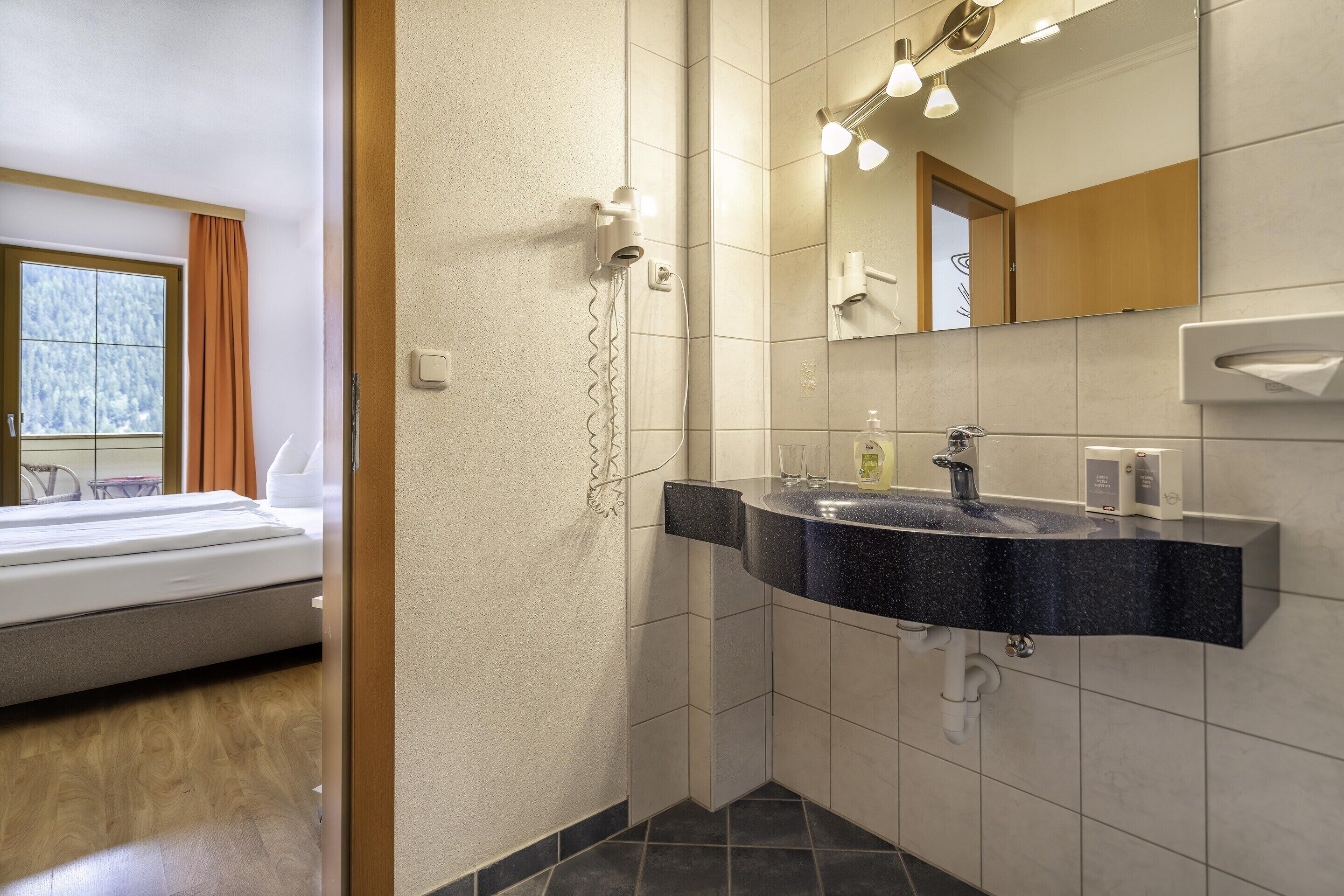 Une salle de bain moderne avec un lavabo noir, un miroir et un sèche-cheveux fixé au mur.