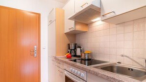 Uma cozinha moderna com porta de madeira, armários brancos, pia de aço inoxidável e forno embutido.