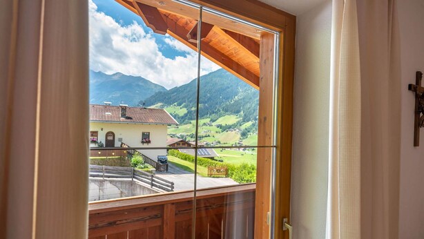 A room with a large window offering a view of a mountain landscape, a wooden balcony, and a cross on the wall. - Apartment Neustift Near Stubai Ski Lift (Neustift Im Stubaital)