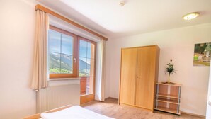 A bedroom with a bed, a wardrobe, a radiator, a window with curtains, and a small table with a plant. - Apartment Neustift Near Stubai Ski Lift (Neustift Im Stubaital)