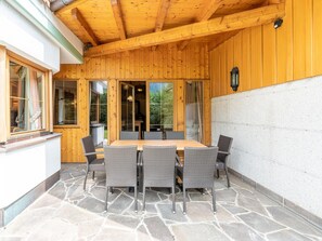 A wooden deck with a stone-tiled floor, a wooden table with chairs, and a glass door leading to a garden. - Charming Holiday Home in Maurach am Achensee (Eben am Achensee)