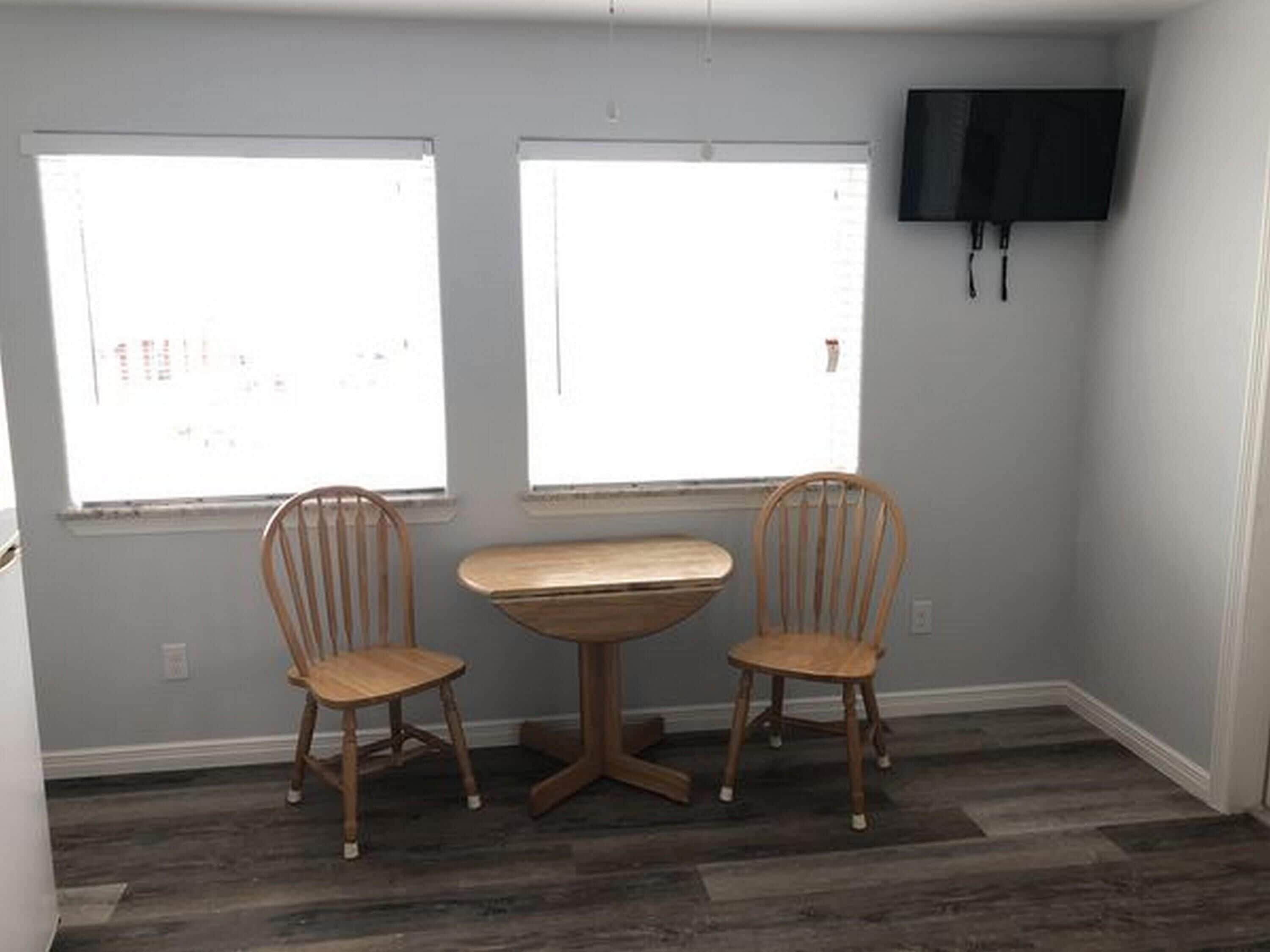 A room with two windows, a wooden table, and two wooden chairs.