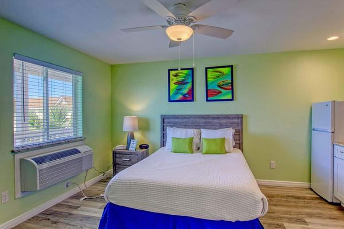 A bedroom with a bed, a ceiling fan, a window with blinds, an air conditioner, and two wall-mounted paintings.