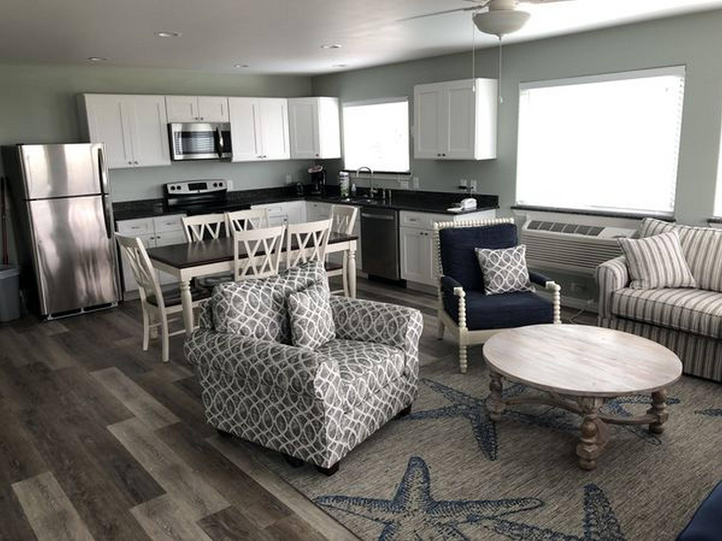 A modern kitchen with white cabinets, stainless steel appliances, and a dining area with patterned furniture.