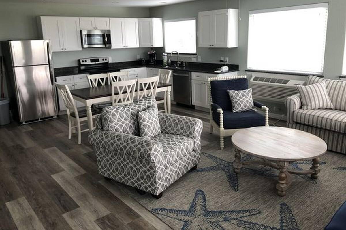 A modern kitchen with white cabinets, stainless steel appliances, and a dining area with patterned furniture.