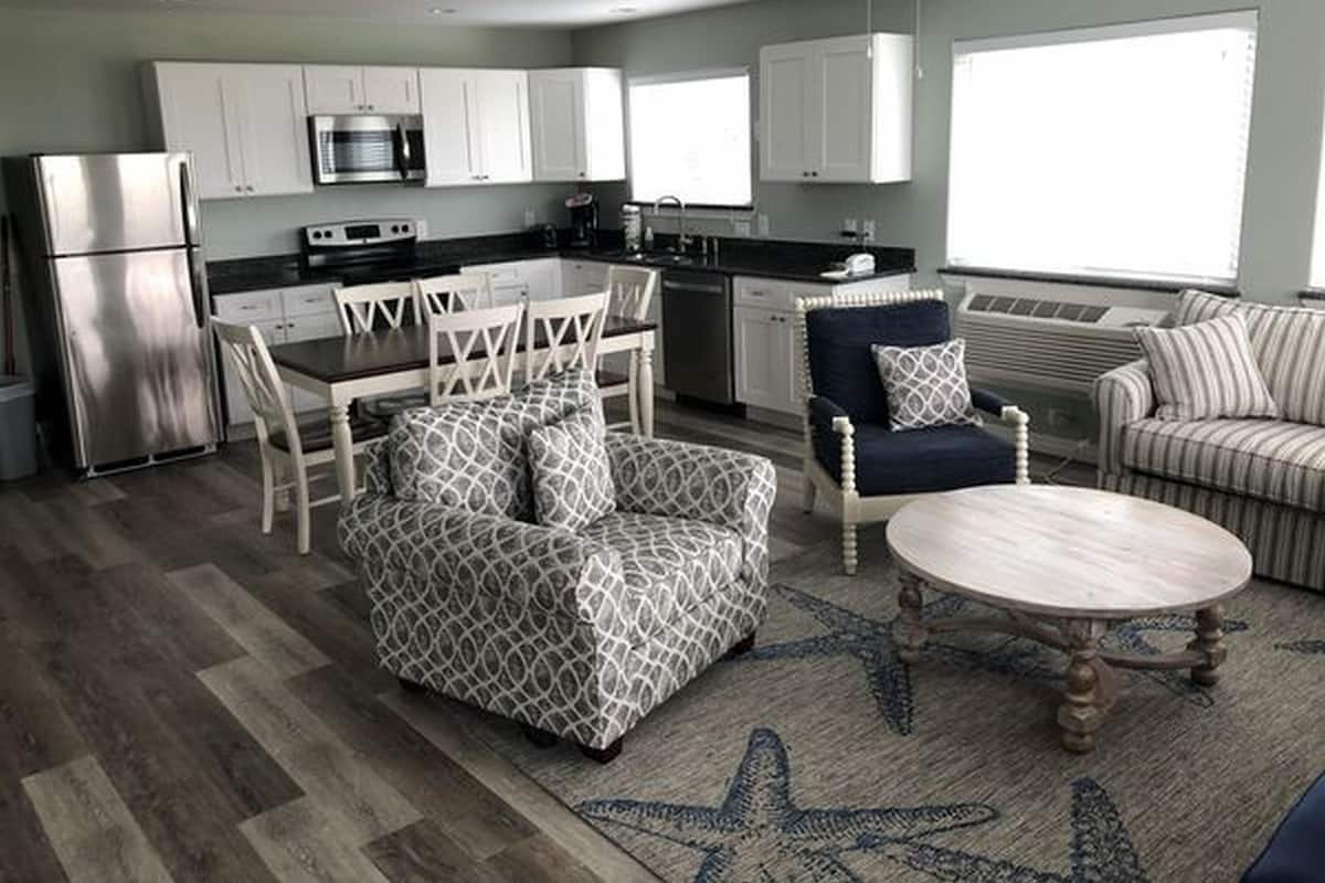 A modern kitchen with white cabinets, stainless steel appliances, and a dining area with patterned furniture.