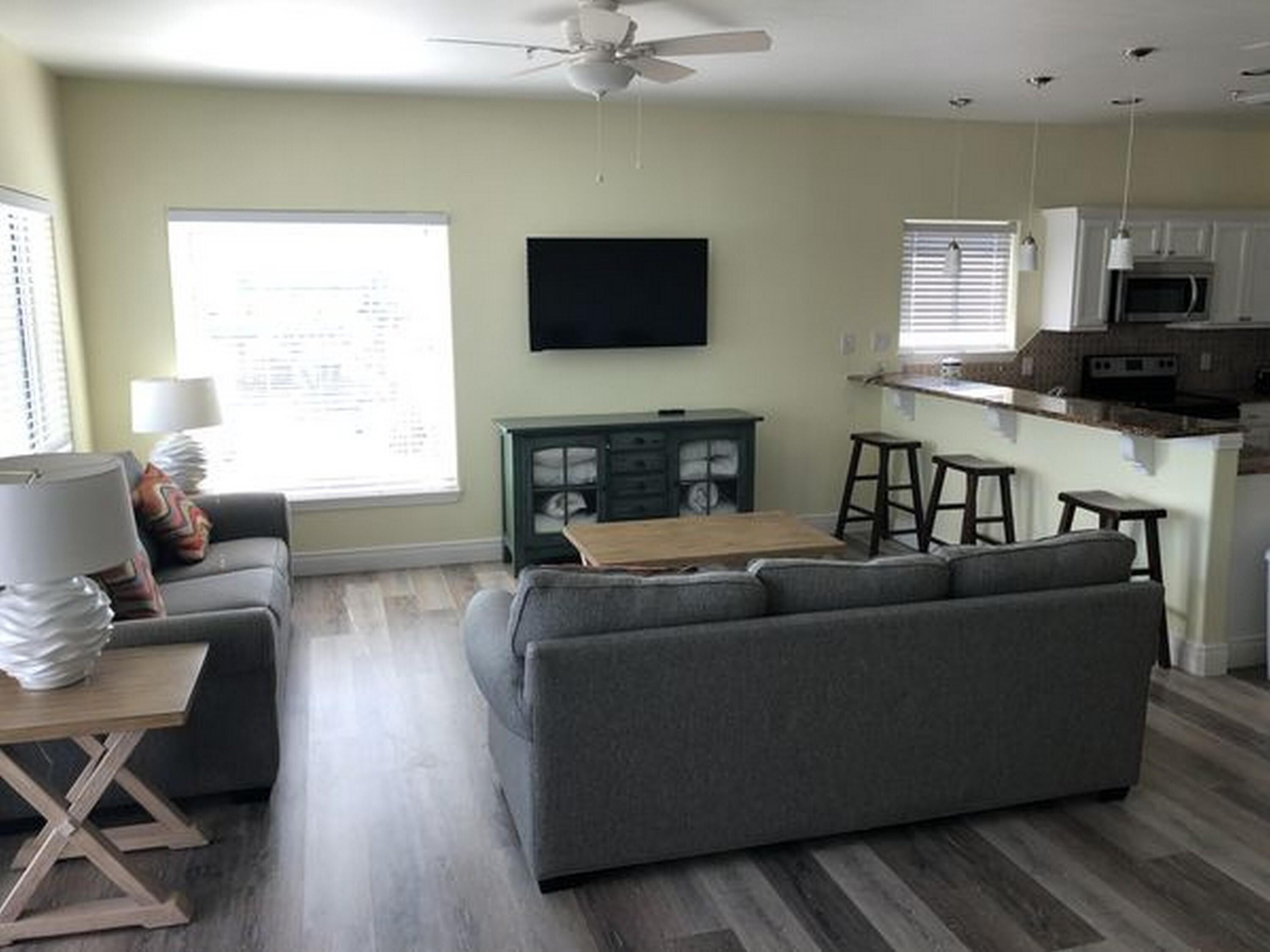 A living room with a sofa, a coffee table, a TV, and a kitchen area with a microwave.