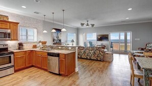 A spacious kitchen with wooden cabinets, a central island, and a dining area with a view. - Beachgate CondoSuites and Oceanfront Resort (Port Aransas)