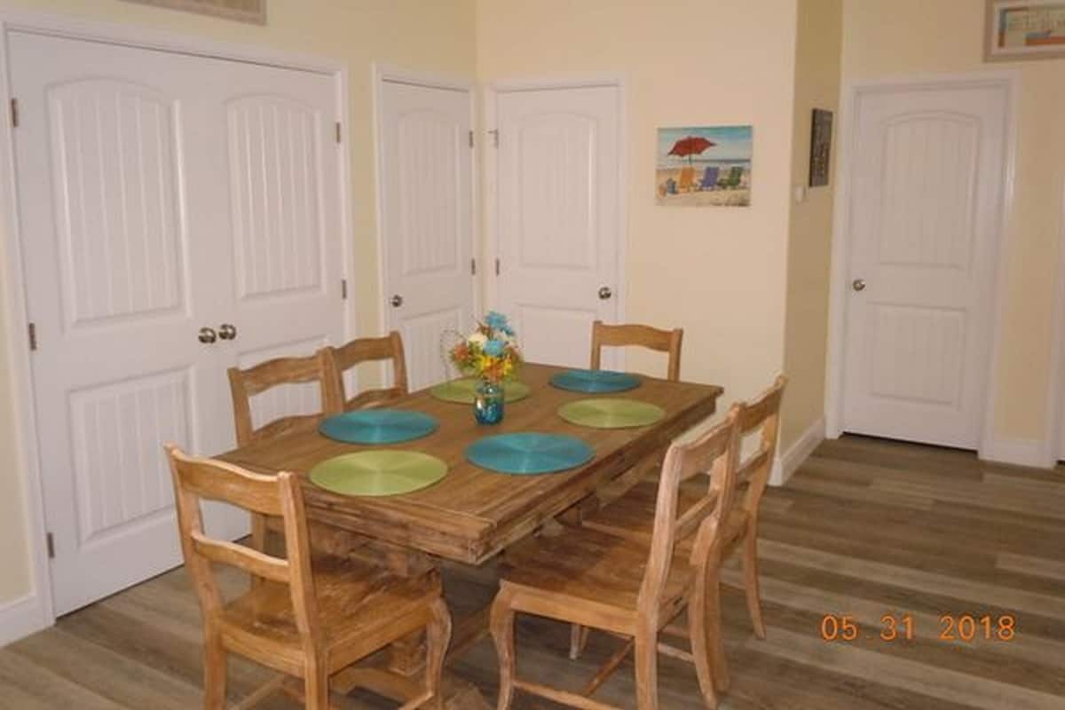 A dining room with a wooden table, four chairs, and a vase of flowers.