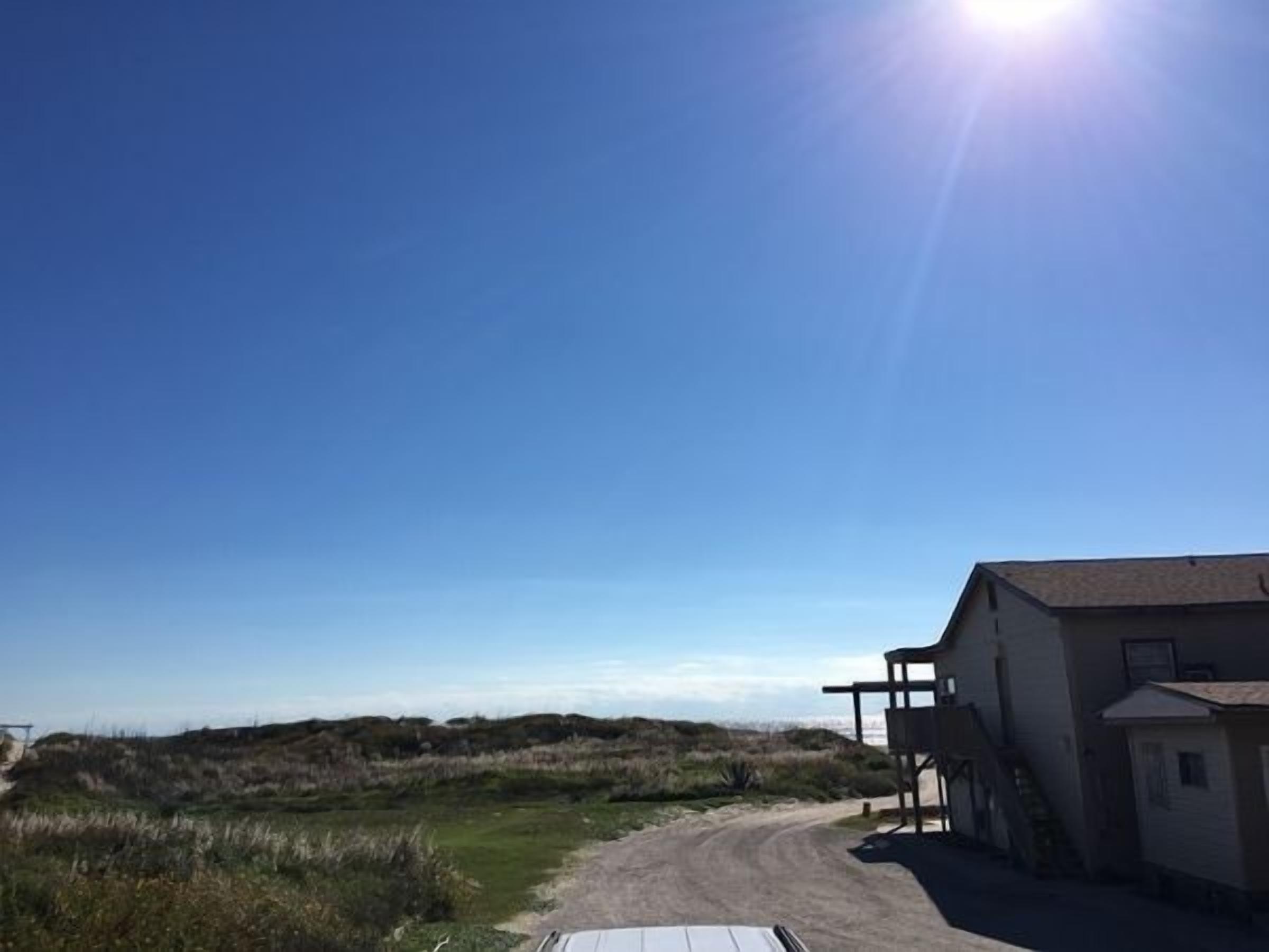 A building with a dirt path leading to it, surrounded by grassy fields and dunes.