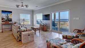 A spacious living room with a sofa, chairs, a table, and a view through large sliding glass doors to the outside. - Beachgate CondoSuites and Oceanfront Resort (Port Aransas)