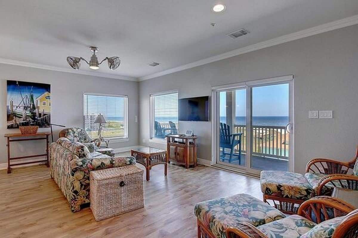 A spacious living room with a sofa, chairs, a table, and a view through large sliding glass doors to the outside.
