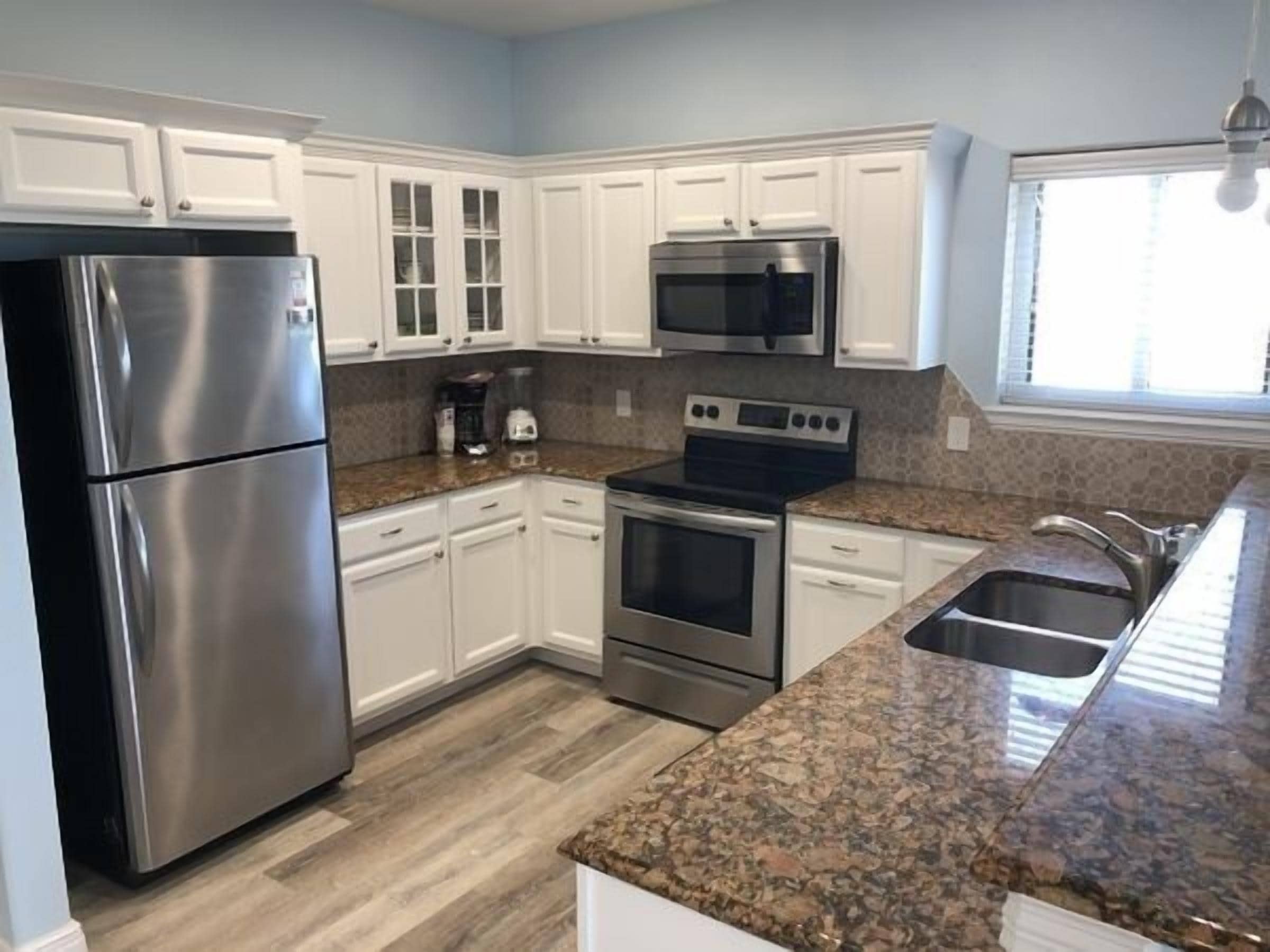 A modern kitchen with white cabinets, stainless steel appliances, granite countertops, and a window providing natural light.